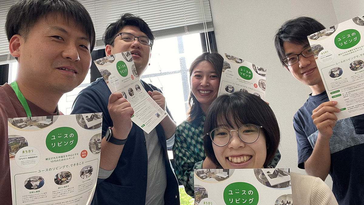 5人の男女が「ユースのリビング」と書かれたパンフレットを持ち、笑顔でポーズ。
