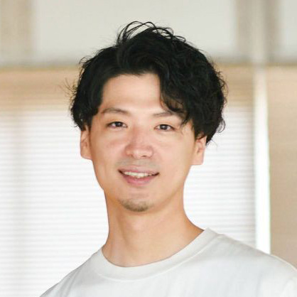 白いシャツの男性が、明るい室内で微笑んでいます。