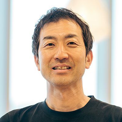 黒いシャツの男性が、明るい室内で微笑んでいます。