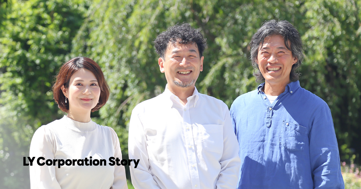 Three people stand smiling against a natural background, creating a bright atmosphere.