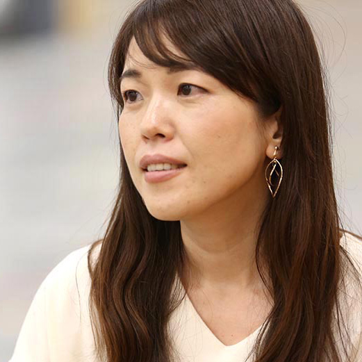 女性が真剣な表情で話している様子。シンプルなイヤリングを着用。