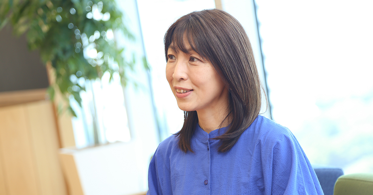 女性がインタビュー中の様子。背景に植物があり、自然光が差し込んでいる。