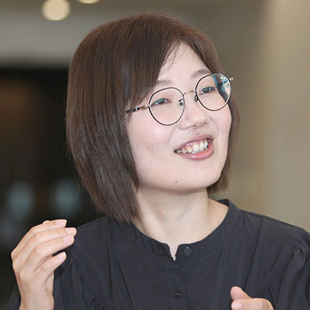 眼鏡をかけた女性が微笑んでいます。彼女は何かを説明しているようです。