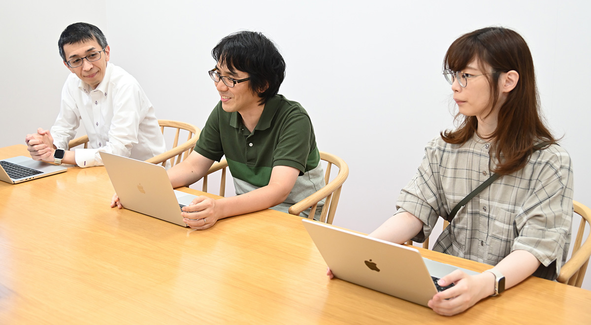3人の人物が会議室でノートパソコンを前にして座っています。リラックスした雰囲気です。