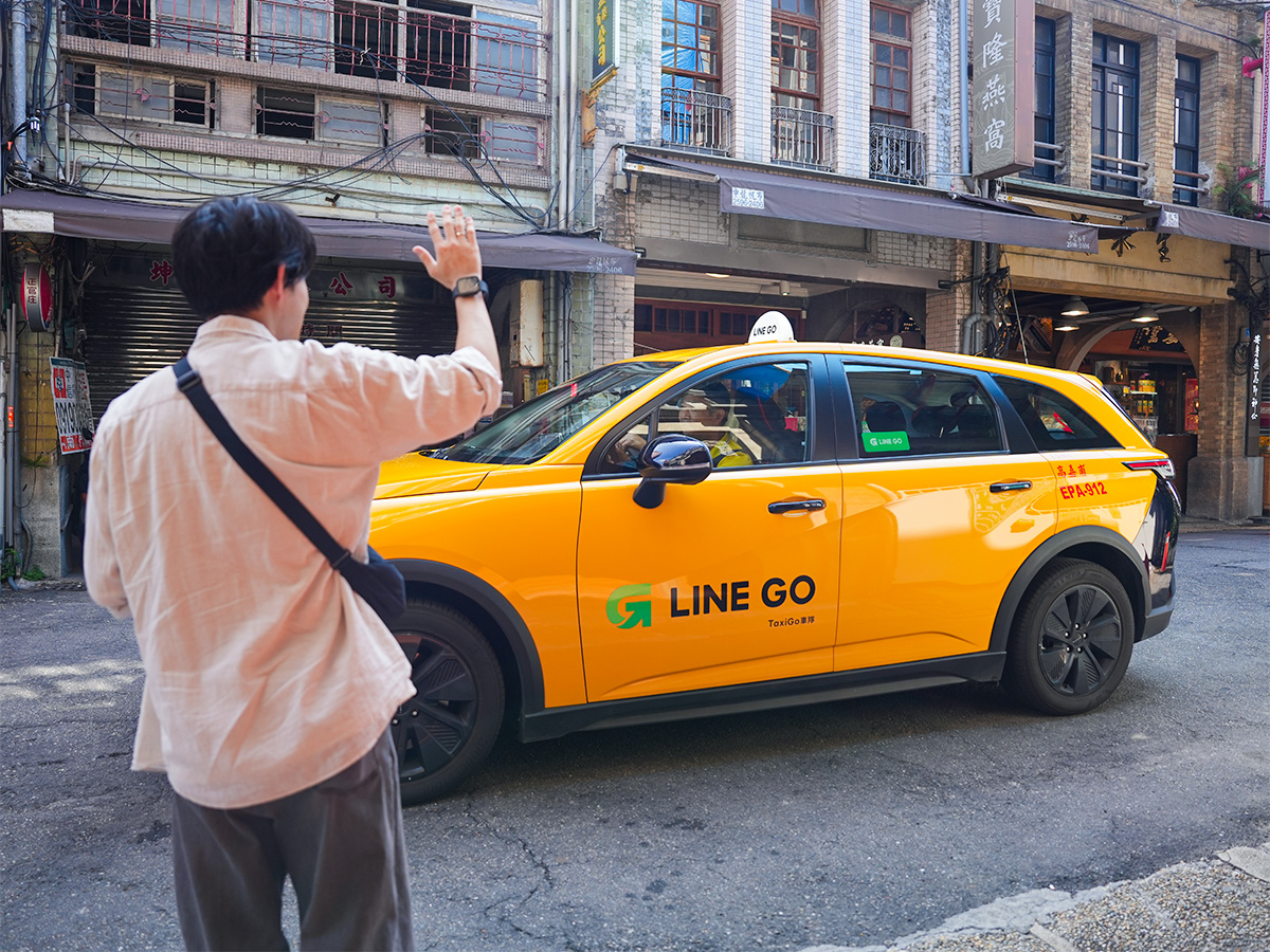 男性が黄色いタクシーを手招きしている写真です。タクシーには「LINE GO」のロゴが描かれています。