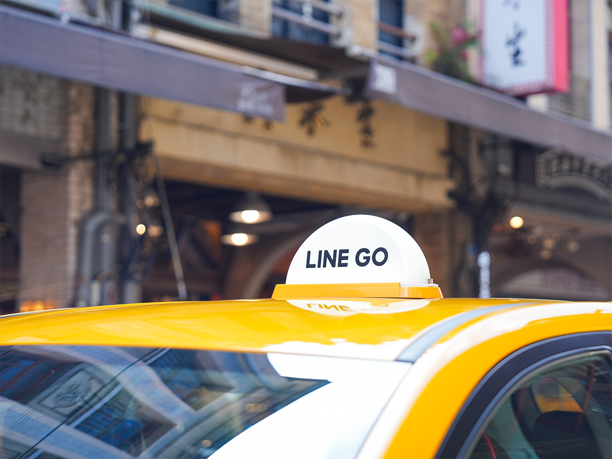 タクシーの屋根に「LINE GO」のサインがある写真です。背景には古い建物が見えます。