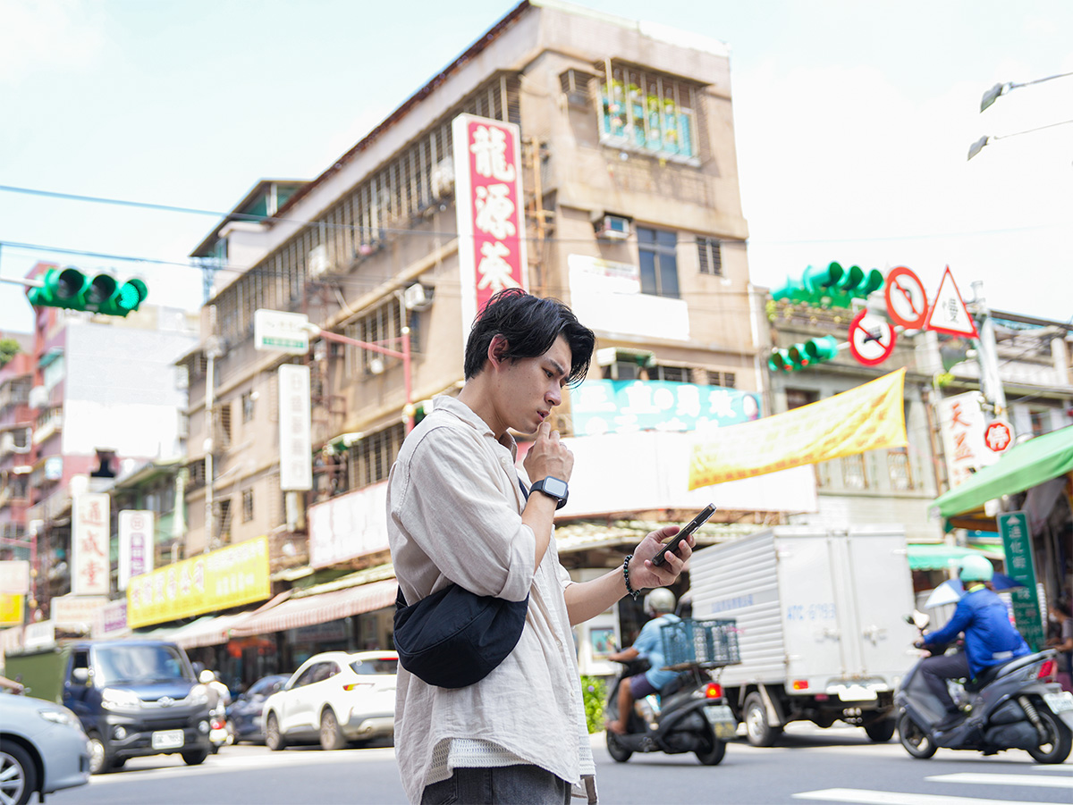 男性が街中でスマートフォンを見ている写真です。周囲には交通が行き交っています。