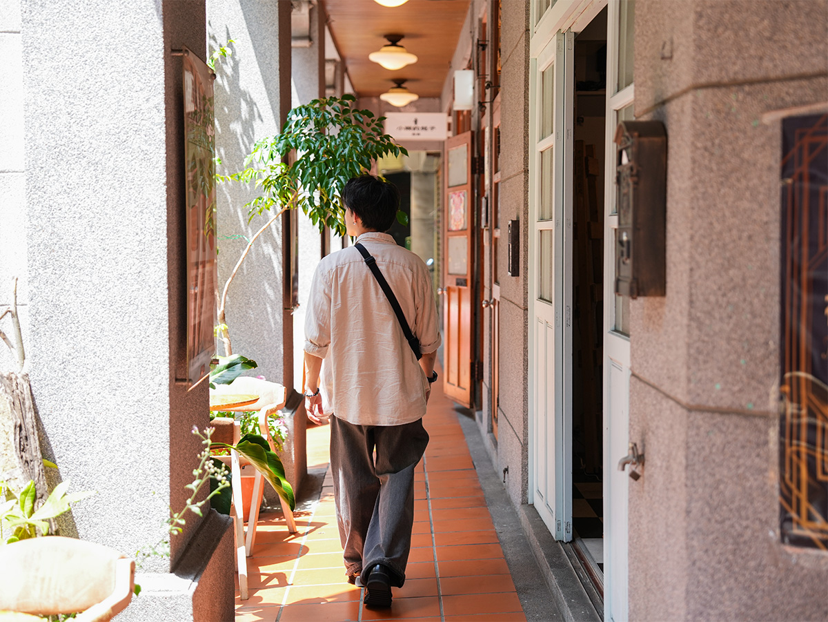 男性が日差しの差し込む廊下を歩いている写真です。両側には植物や装飾が見えます。