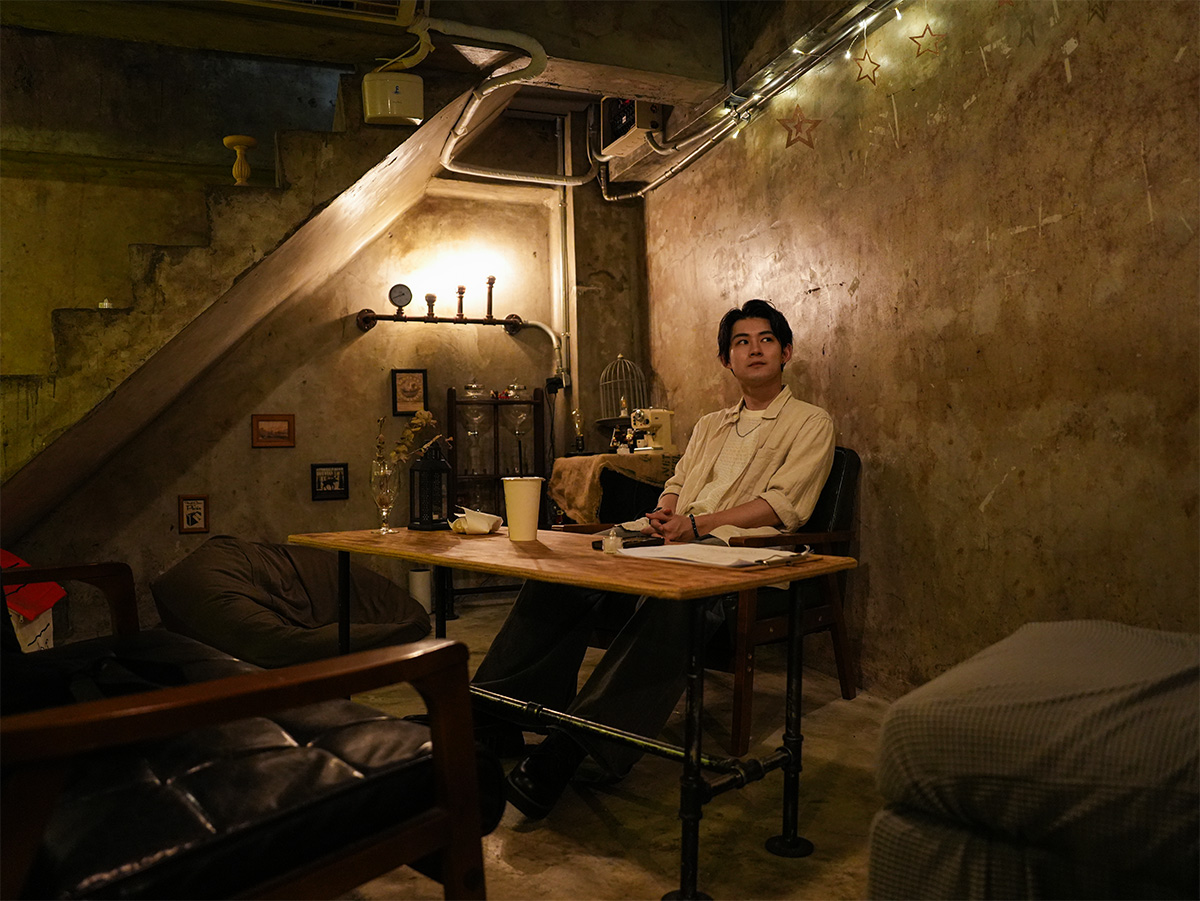 男性が落ち着いた雰囲気のカフェでくつろいでいる写真です。薄暗い照明が心地よさを演出しています。