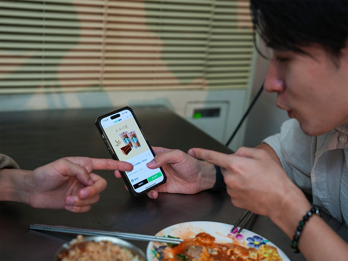 テーブルの上にスマートフォンがあり、二人が画面を指差しながら何かを話しています。料理も見えます。