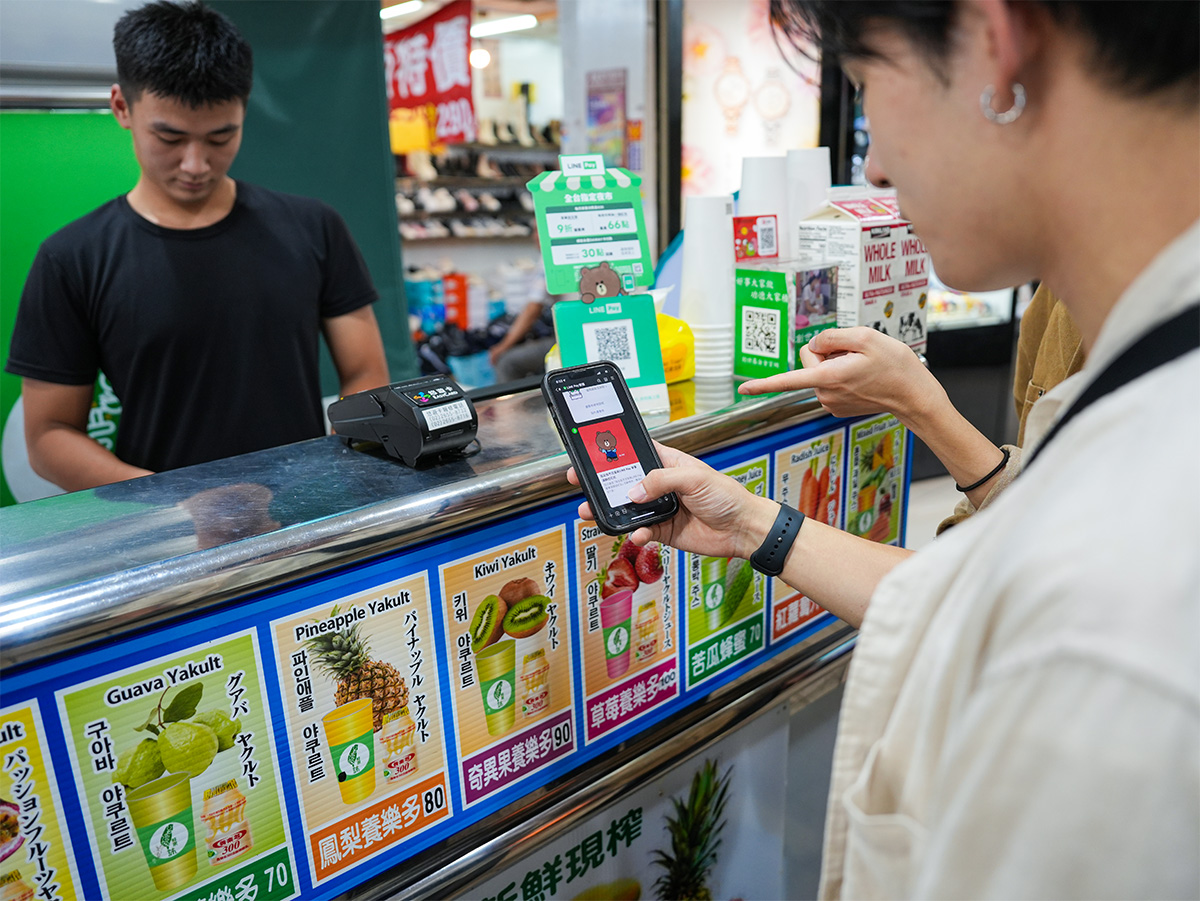 カウンターでスマートフォンを提示し、支払いを行っている様子が見られます。店員が対応しています。