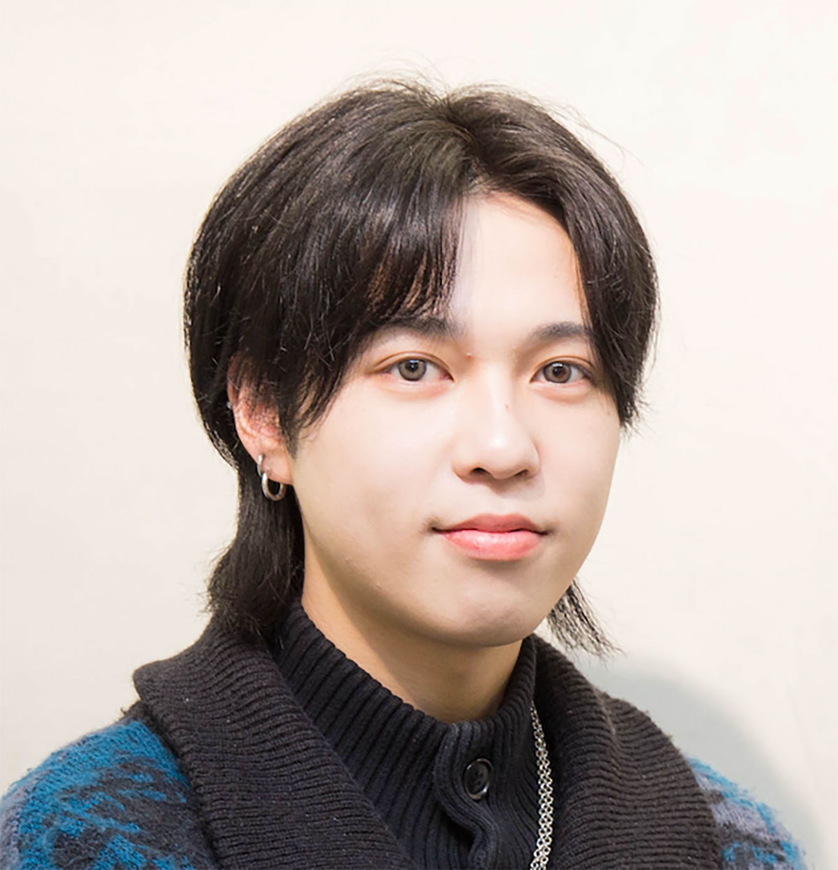 若い男性が微笑んでいる写真です。彼はカジュアルな服装で、耳にピアスをつけています。