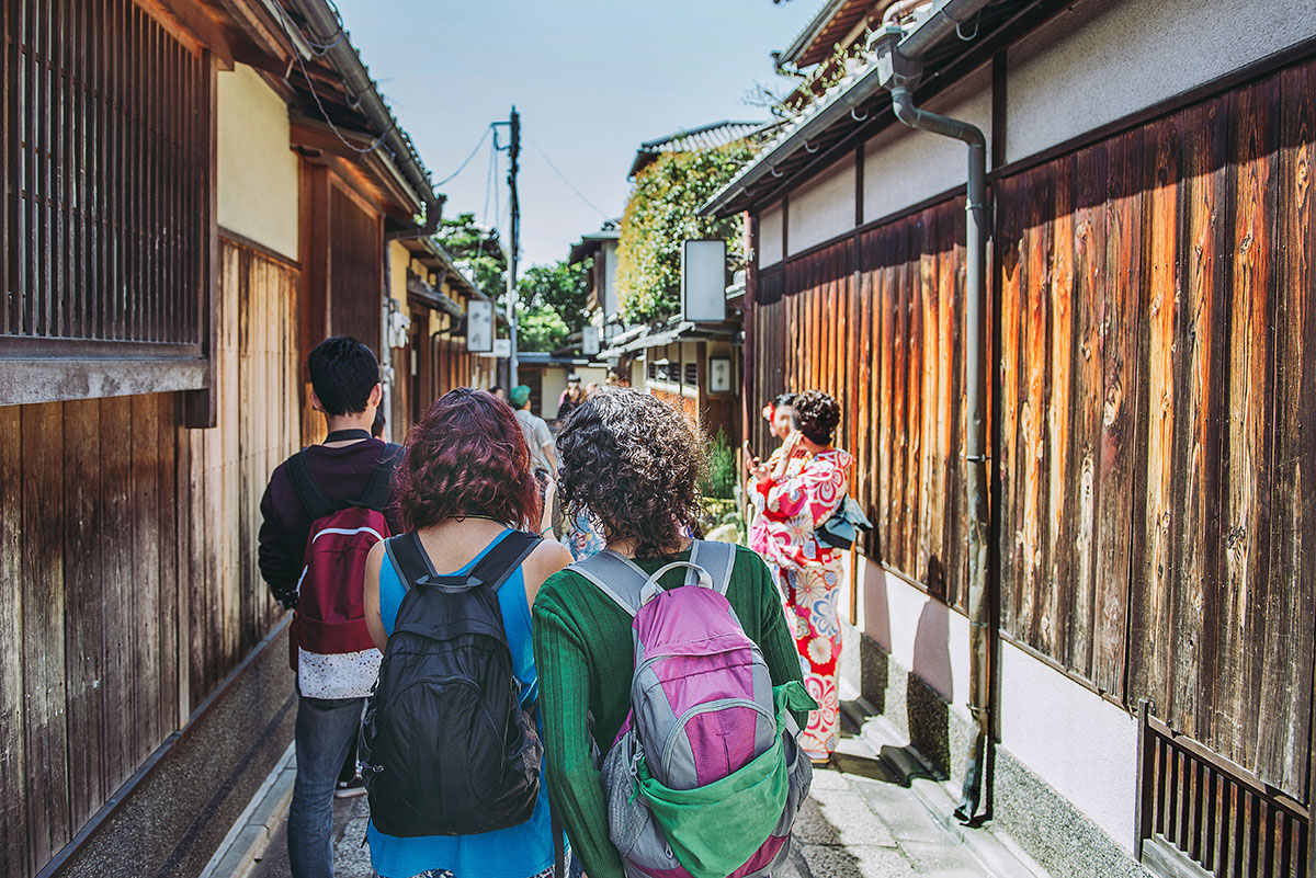 木造の伝統的な街並みを歩く観光客たちの後ろ姿が写っています。