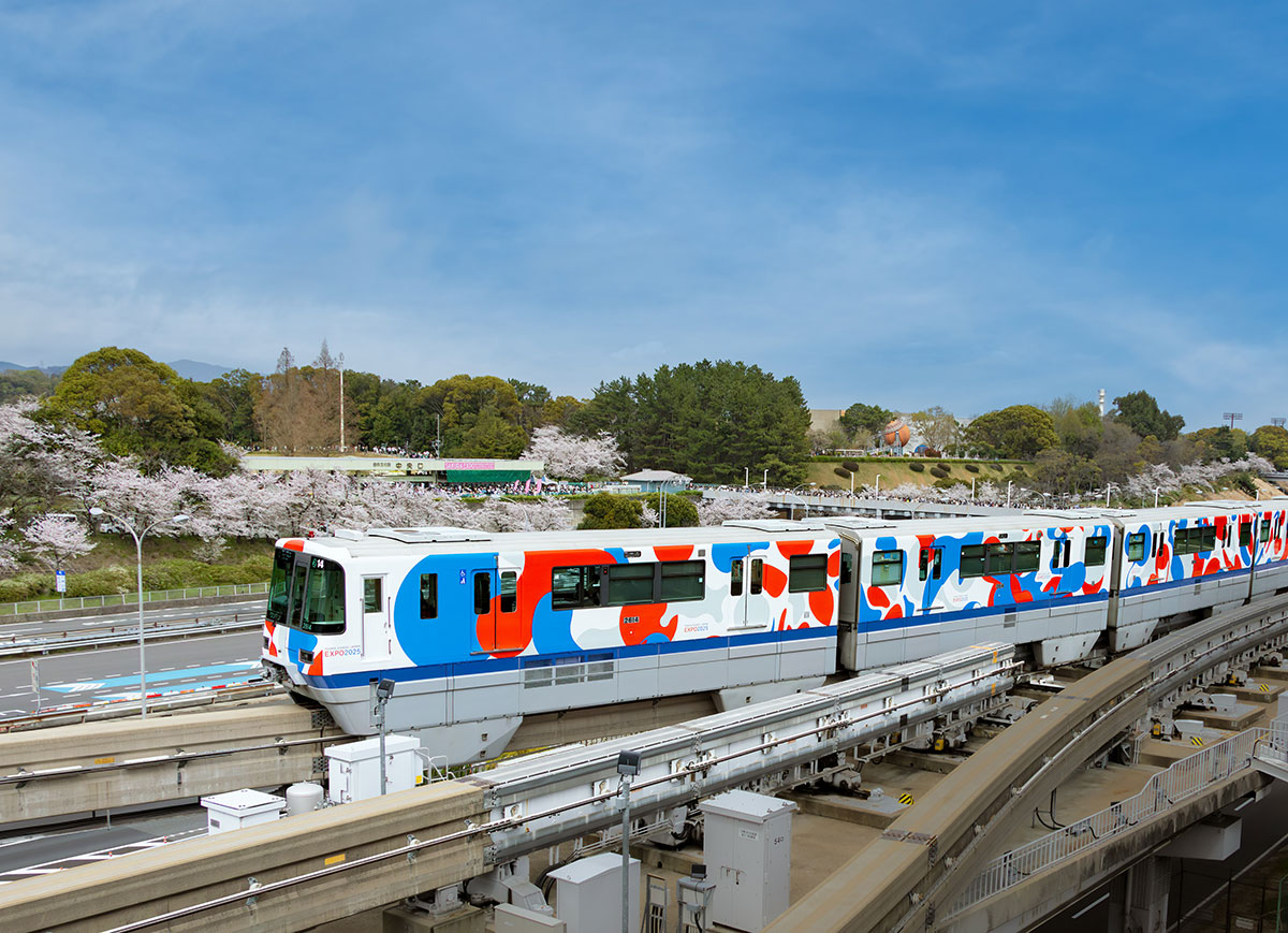 カラフルなデザインの列車が桜の木々の間を走行している様子です。