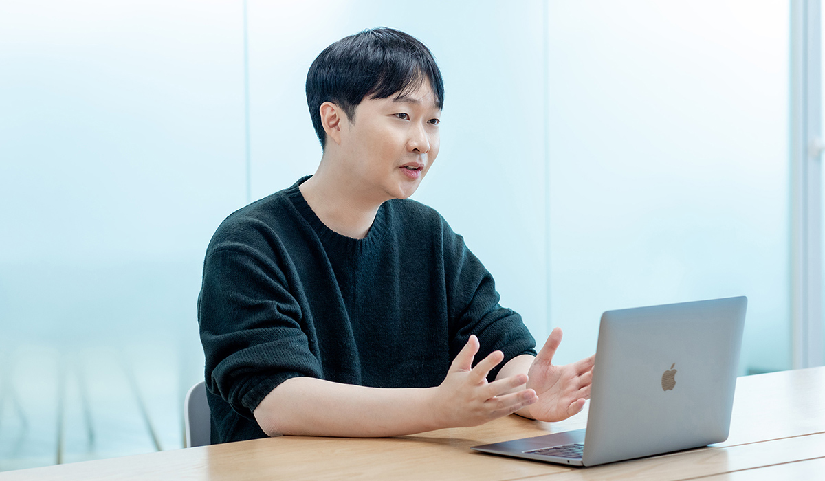 同じ男性がノートパソコンを前に、手を使って説明している場面。