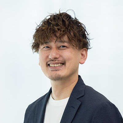 男性が笑顔でカメラを見つめている。白い背景に、カジュアルなジャケットを着ている。