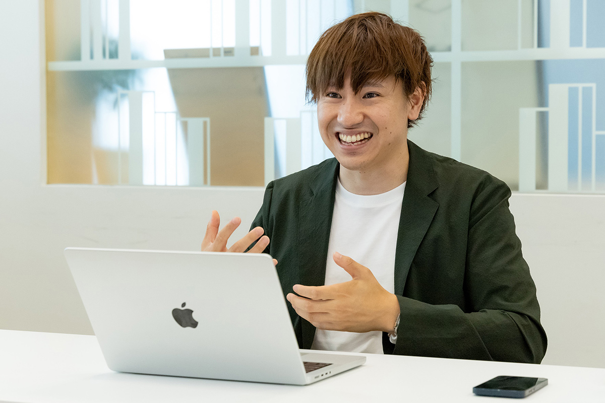 男性がノートパソコンの前で話をしている写真です。彼は笑顔で手振りを交えています。