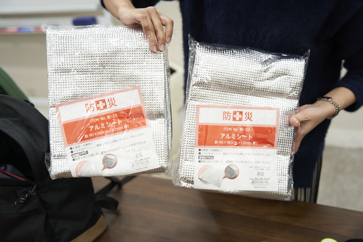 防災用のアルミシートが2つ、手で持たれています。パッケージにはサイズと用途が記載されています。