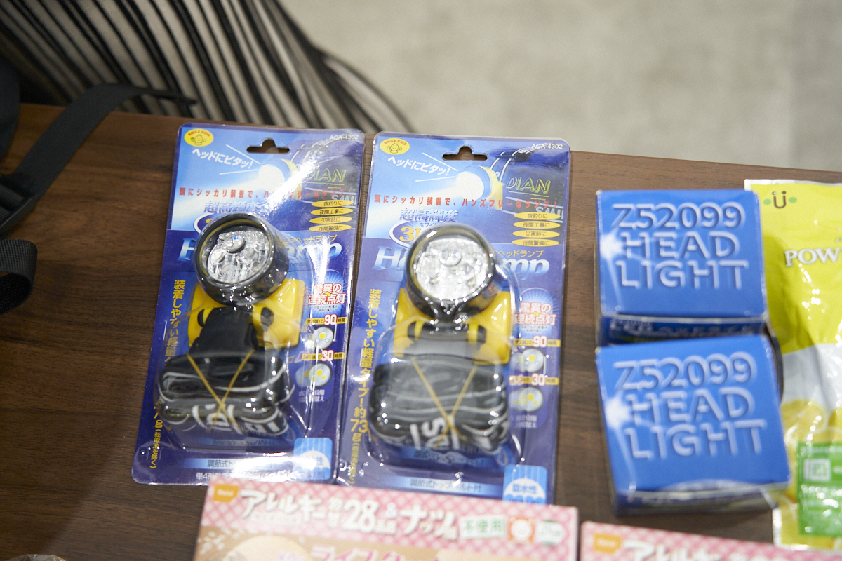 テーブルの上にヘッドライトが複数置かれています。パッケージには使用方法や特長が記載されています。防災用品の一部として並べられています。