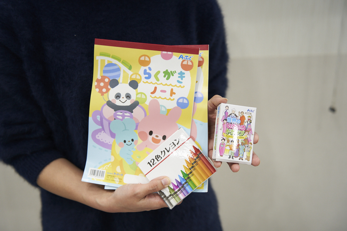 女性がらくがきノートと12色クレヨンを持っています。ノートには動物のイラストが描かれています。