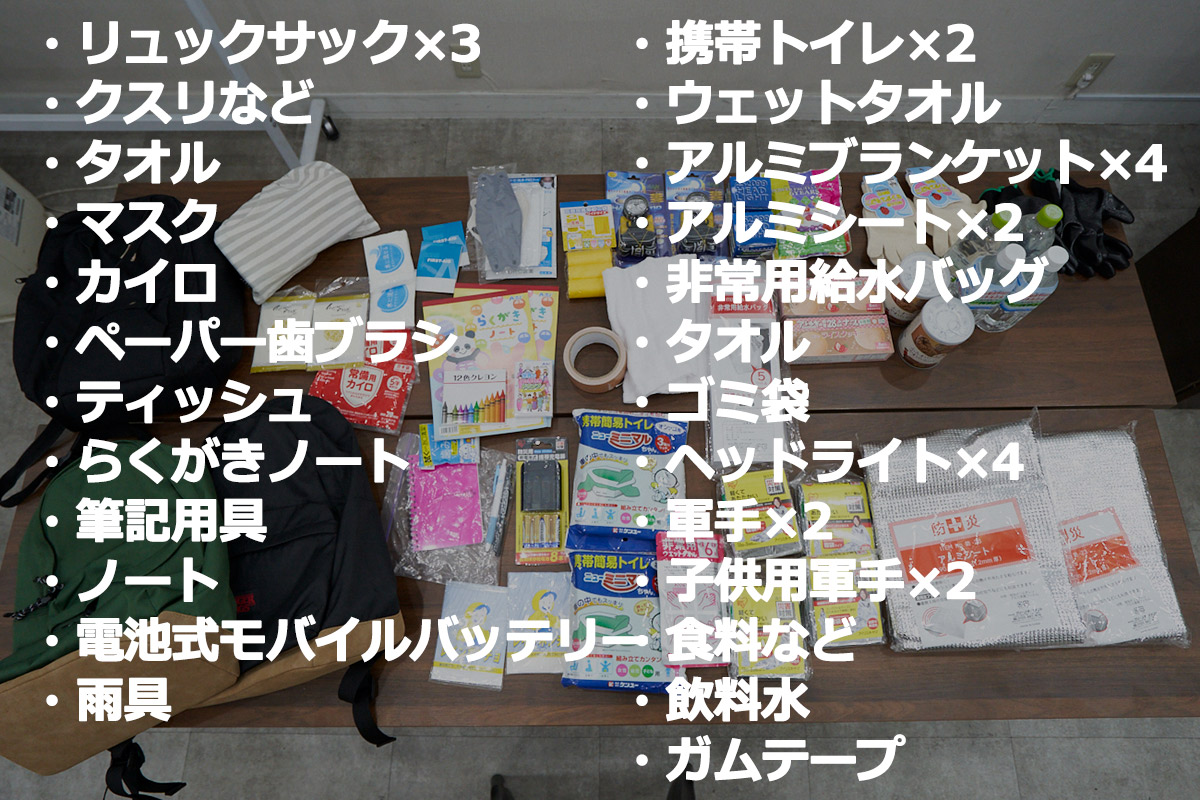 この画像は、非常時に備えた防災グッズの一覧です。リュック、食料、携帯トイレ、飲料水などが並べられています。