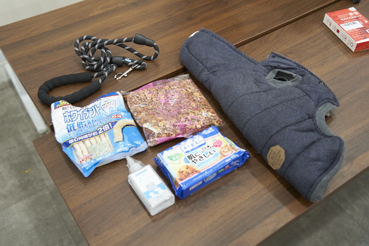 ペット用品がテーブルに並んでいます。リード、ペットフード、ウェットティッシュ、ペット用ウェアなどが見えます。