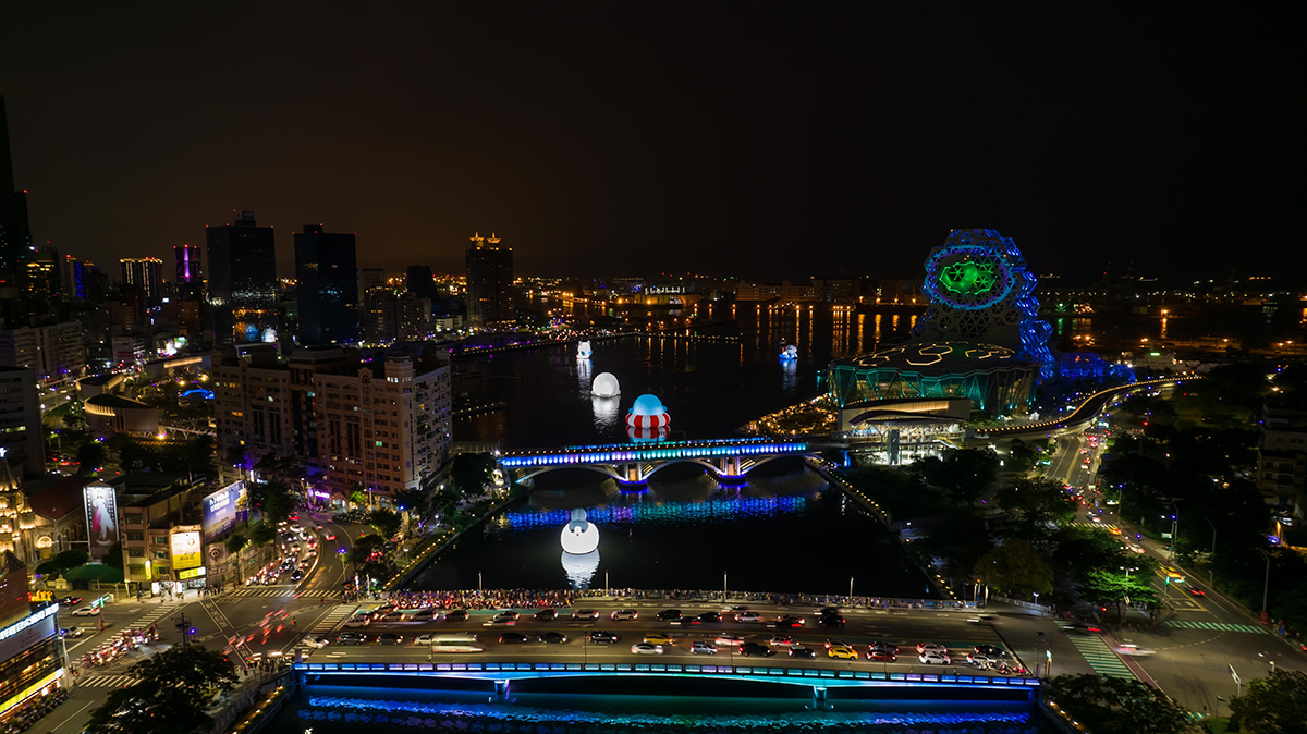 夜の都市の風景を上空から撮影した写真です。川沿いにライトアップされた建物や橋があり、街の活気が感じられます。