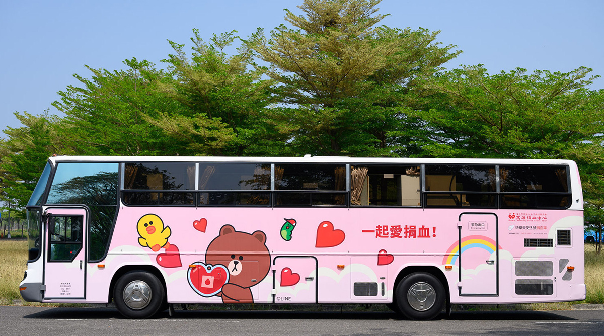 LINE FRIENDSキャラクターが描かれたピンク色のバスが、献血を促進するメッセージと共に停車しています。
