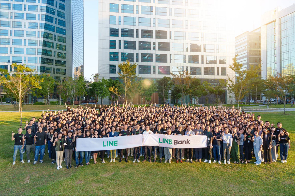 大勢の人々が「LINE Bank」と書かれた横断幕を持ち、オフィスビルの前で集まっている集合写真です。