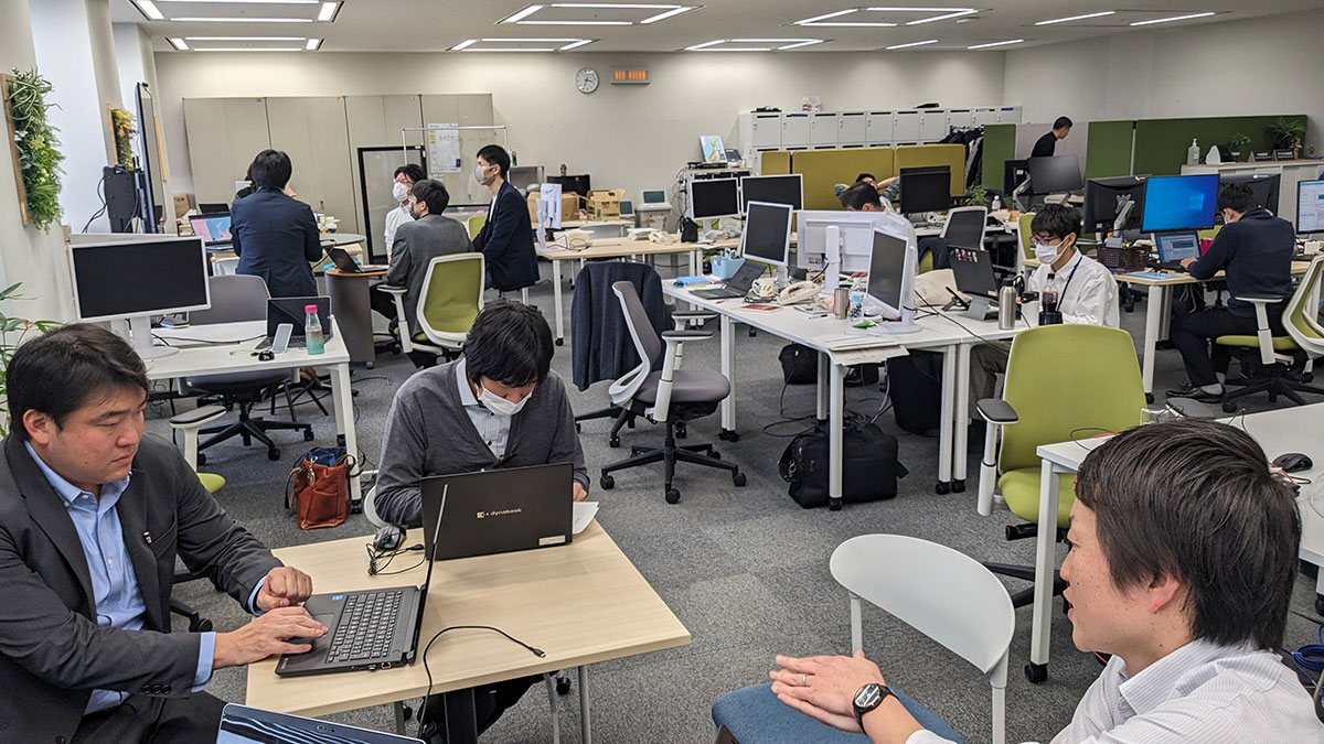 オフィス内で働く人々。パソコンを使って作業をする社員たちが見えます
