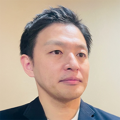 スーツを着た男性・谷場さんのポートレート。短髪で真剣な表情をしています