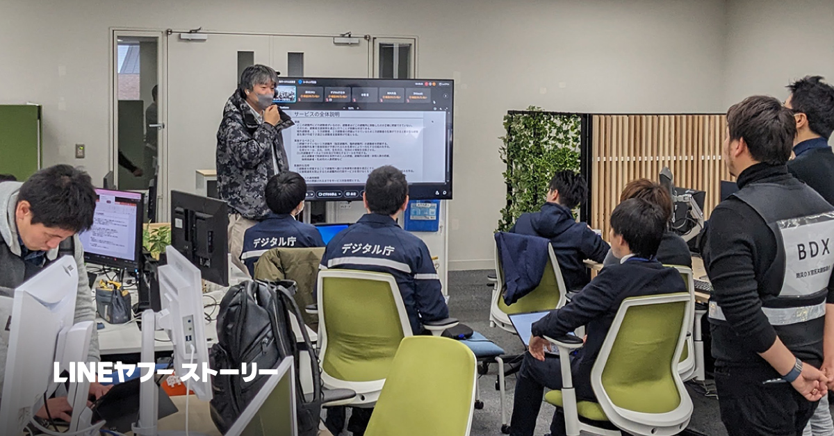 会議室でプレゼンテーションを行う人々。デジタル庁のジャケットを着た参加者が注目しています