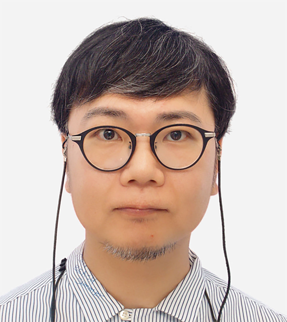 丸眼鏡をかけた男性・米倉のポートレート。ストライプのシャツを着ています