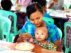 母親に給食を食べさせてもらう子ども