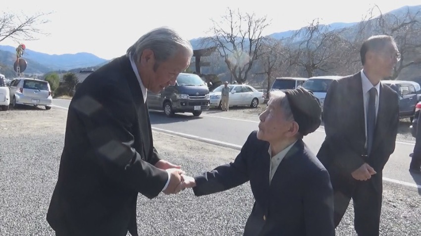 固く握手する佐藤ハルエさん（右）と碑文建立に尽力した藤井宏之さん