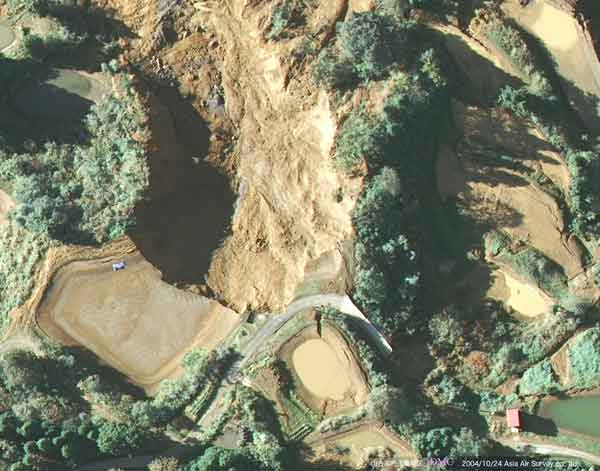 山古志村虫亀地区：崩壊により養殖池が決壊し、水が完全に失われている。流下した土砂が住宅と道路を押し流した。（2004年10月24日撮影）