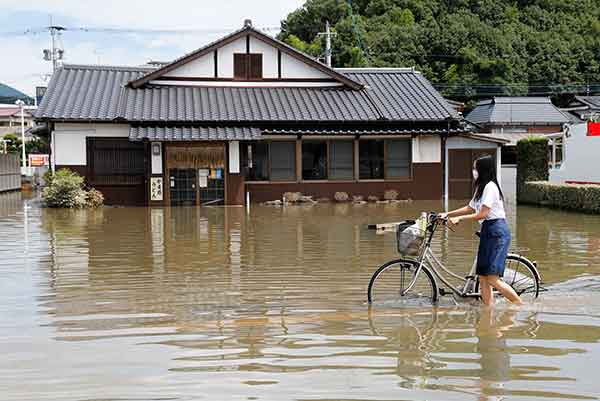 浸水した道で自転車を押す女性＝2021年8月15日、佐賀県武雄市